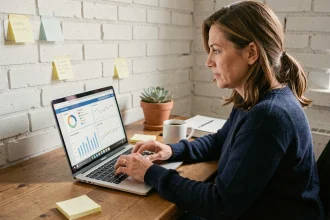 Femme entrepreneur travaillant seule sur une stratégie digitale depuis son bureau à domicile avec un laptop affichant des tableaux de bord analytiques