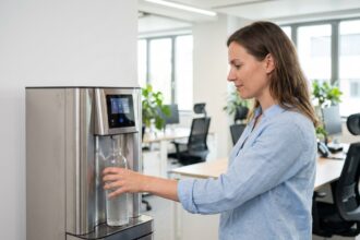 Femme remplissant une bouteille à une fontaine à eau en inox dans un bureau moderne, illustration de la location ou achat de fontaine à eau en entreprise
