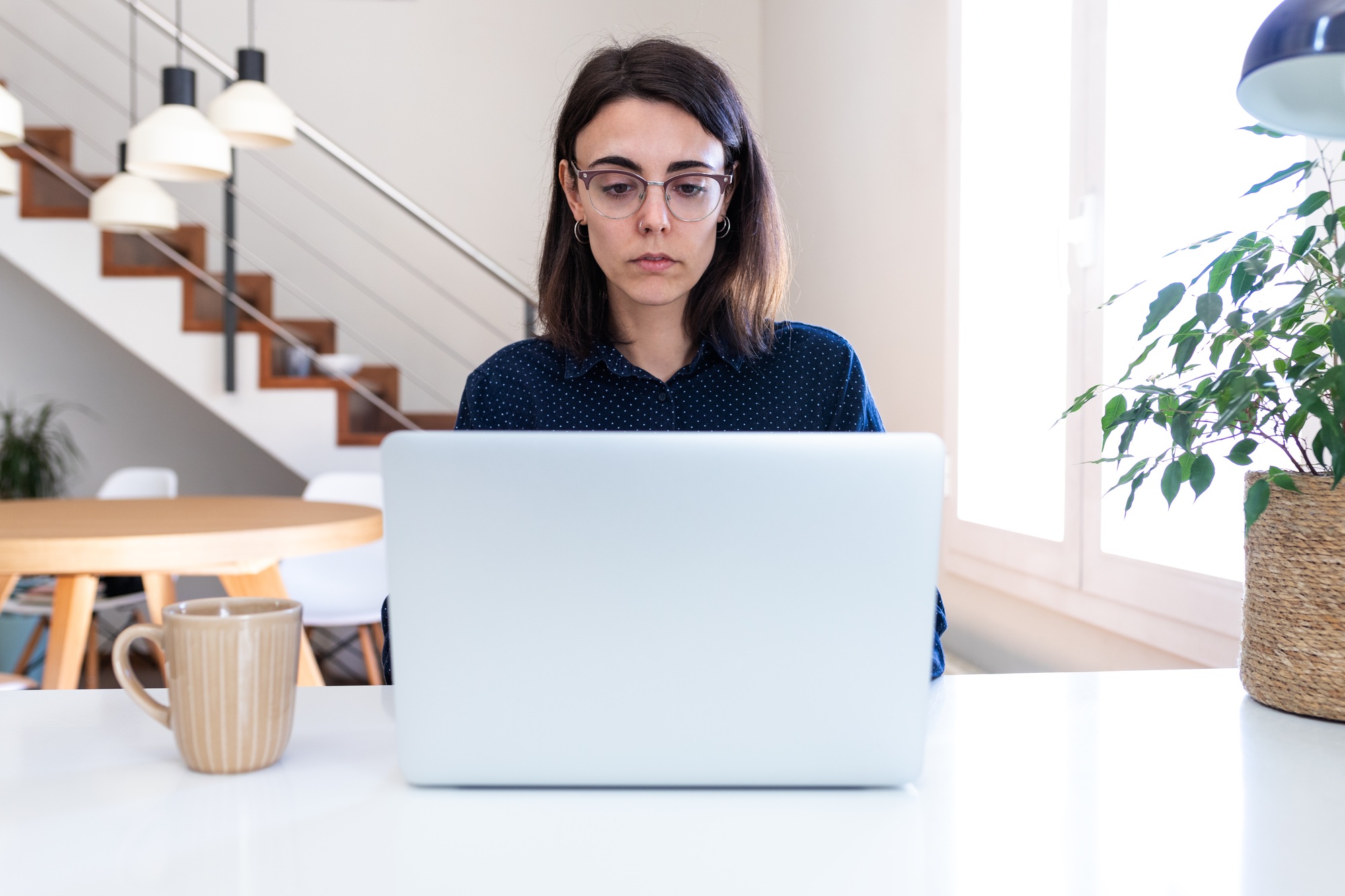 Young woman with glasses working with laptop at home. Female freelancer using computer at office.